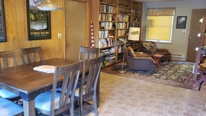 A dining area with a wooden table and chairs, a bookshelf, and a rug.