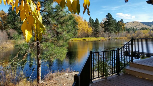 A wooden deck overlooking a calm lake with surrounding trees and hills.