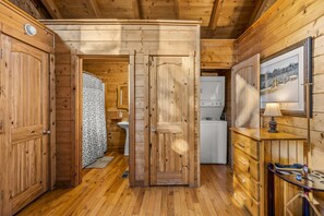 L’intérieur d’une cabane en bois, avec une porte en bois, un évier, un petit réfrigérateur et un tableau encadré accroché au mur.
