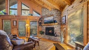 Una sala de estar acogedora con chimenea, sofá de cuero, vigas de madera y ventanas amplias.