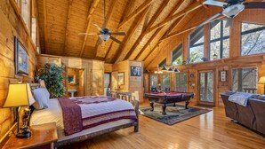 Una habitación amplia con techo de madera, una cama, una mesa de billar y un sofá.