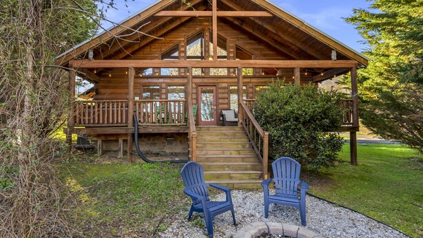 Una cabaña de troncos con un porche, dos sillas Adirondack y un pequeño jardín.