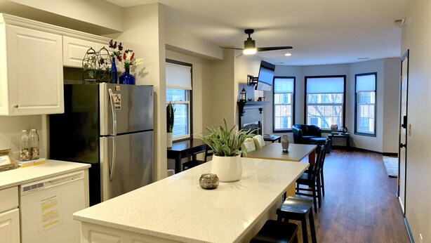 Una cocina moderna con armarios blancos, un refrigerador de acero inoxidable, una isla central con asientos y ventanas grandes que ofrecen luz natural.