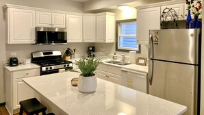 Una cocina moderna con armarios blancos, electrodomésticos de acero inoxidable, encimera de granito y una planta en maceta.