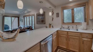 A modern kitchen with wooden cabinets, a dishwasher, and a large window. - Cozy Creekside Retreat • Walk to Main Street • Mountain Views & Fireplace (Frisco)