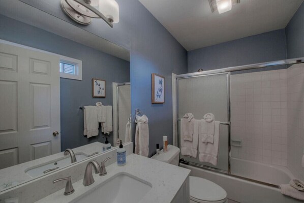 A bathroom with a large mirror, a double sink, a toilet, and a walk-in shower.