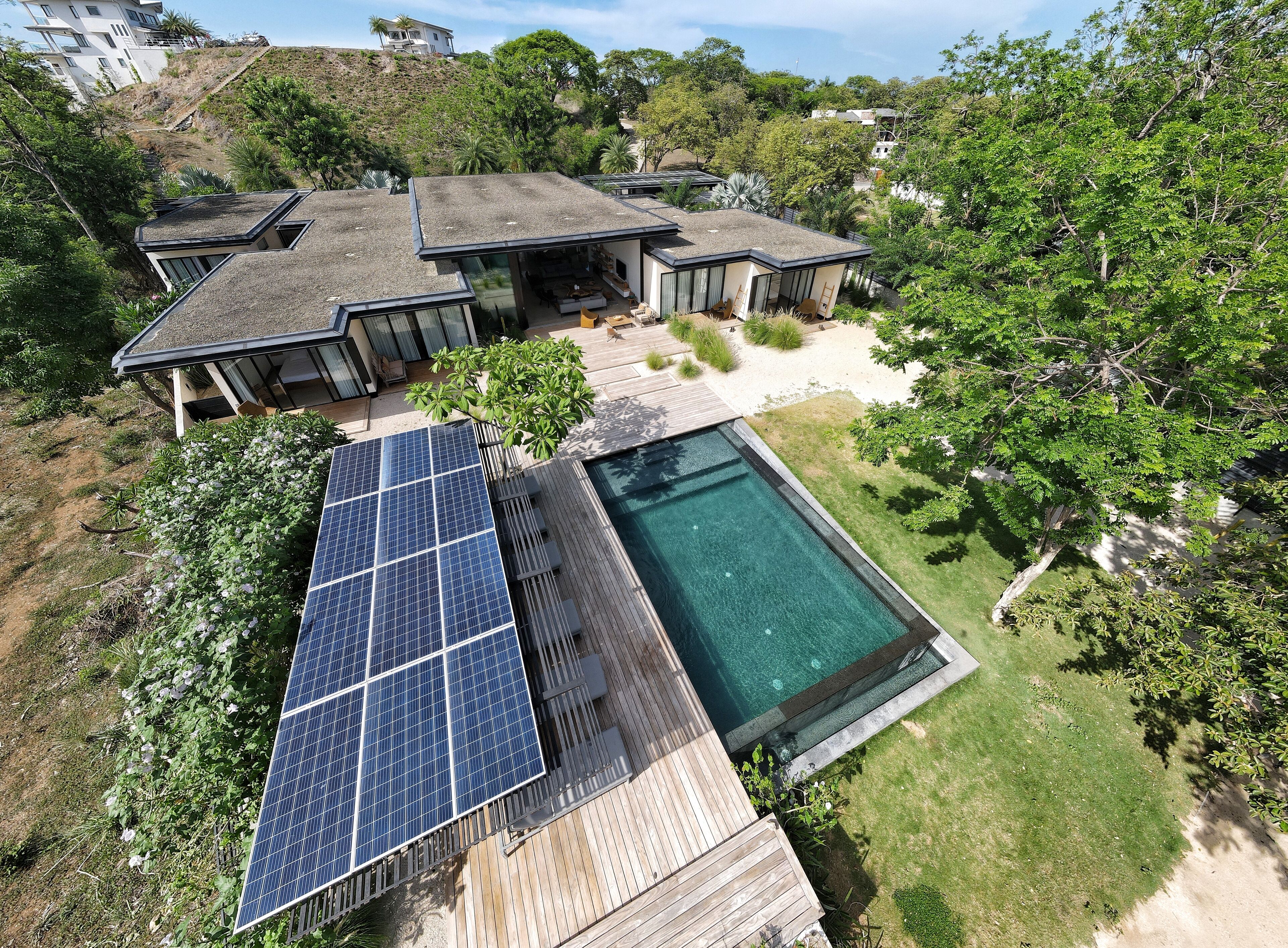 A modern house with a swimming pool, solar panels, and a lush garden.