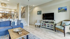 Ein großzügiges Wohnzimmer mit blauem Sofa, einem Holztisch, einem Korbstuhl und einem Fernseher auf einer Holzkommode.