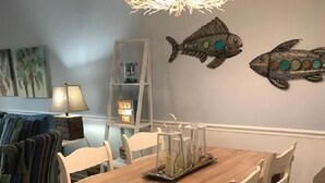 A dining room with a wooden table and chairs, a chandelier, and decorative fish on the wall. - Seacoast Gardens lll Oceanfront Complex. NON DRIVING Beach. DIRECT OWNER BOOKING (New Smyrna Beach)