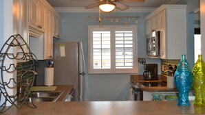 A kitchen with white cabinets, a ceiling fan, a window with blinds, a refrigerator, and a microwave. - Seacoast Gardens lll Oceanfront Complex. NON DRIVING Beach. DIRECT OWNER BOOKING (New Smyrna Beach)