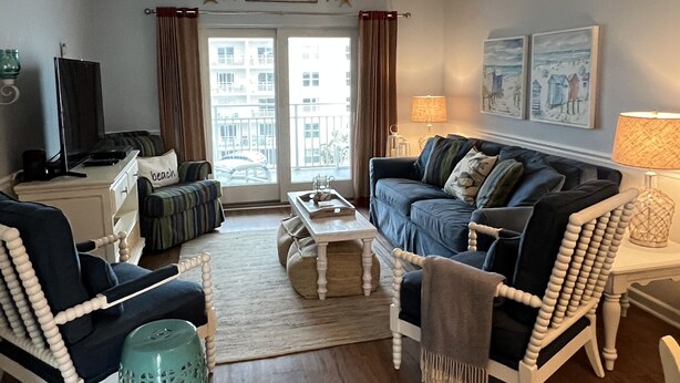 A living room with a sofa, armchairs, a coffee table, and a TV. There is a window with curtains, artwork on the wall, and a sign that says "BEACH". - Seacoast Gardens lll Oceanfront Complex. NON DRIVING Beach. DIRECT OWNER BOOKING (New Smyrna Beach)