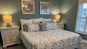 A bedroom with a bed, two nightstands, two wall-mounted lamps, and two framed pictures. - Seacoast Gardens lll Oceanfront Complex. NON DRIVING Beach. DIRECT OWNER BOOKING (New Smyrna Beach)