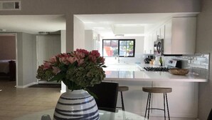 Eine moderne Küche mit weißen Schränken, einer zentralen Kochinsel und einem Blumenstrauß auf einem Tisch.