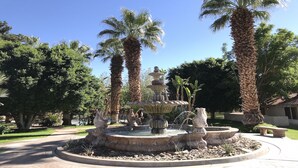 Ein mehrstufiger Brunnen mit Statuen, umgeben von Palmen und anderer Vegetation in einer angelegten Grünfläche.