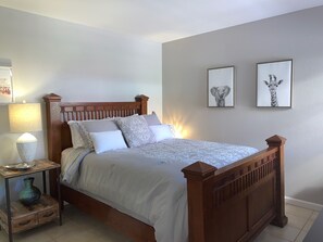 Un dormitorio con una cama de madera, una mesita de noche con lámpara y dos cuadros enmarcados en la pared.