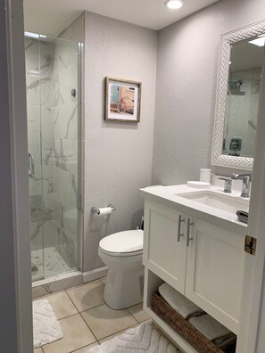 Un baño con cabina de ducha de vidrio, inodoro, lavabo con espejo y un cuadro enmarcado en la pared.