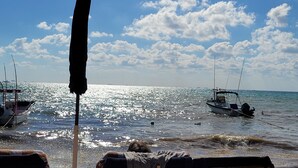 A beach scene with boats, a clear sky, and a bright sun reflecting on the water.