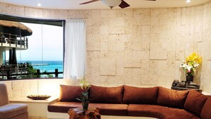 A modern living room with a curved brown sofa, a wooden coffee table, and a view of the ocean through large windows.