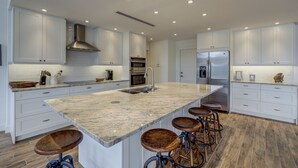 Cocina moderna con muebles blancos, una isla grande con taburetes, electrodomésticos de acero inoxidable y suelo de madera.
