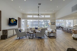 Relax in this open-plan living area with a high ceiling, ceiling fan, and large windows.