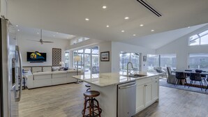 Una cocina amplia con una isla central, un comedor con mesa y sillas, y una sala de estar con sofá y televisor.