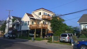 Une maison à deux étages avec un balcon, des voitures garées et un poteau électrique.