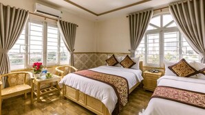 Habitación de hotel con dos camas, piso de madera, una mesita con un florero y un equipo de aire acondicionado.