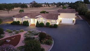 Une maison à deux étages avec un garage, entourée de jardins aménagés et dotée d’une allée.