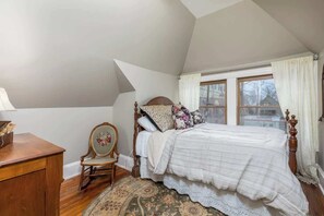 Une chambre à coucher avec un lit en bois, un fauteuil à bascule, un bureau et une grande fenêtre avec des rideaux.