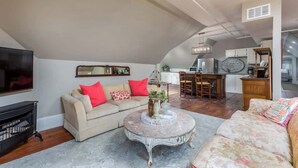Un espacio habitable amplio con techo alto, un conjunto de sofás, una mesa de centro y una cocina al fondo.