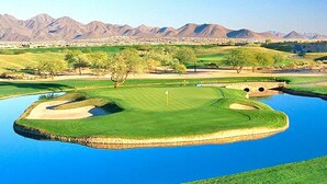 Un parcours de golf avec des obstacles d’eau, des arbres et des montagnes en arrière-plan.