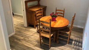 Un comedor con una mesa redonda de madera, seis sillas de madera, un aparador de madera y una lámpara colgante.