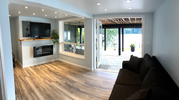 Una sala de estar moderna con piso de madera, televisor integrado y un ventanal amplio.