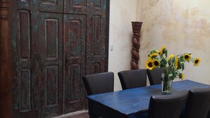 Ein Essbereich mit einem blauen Tisch, schwarzen Stühlen, einer Vase mit Sonnenblumen und einer rustikalen Holztür.