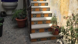 Eine Treppe mit gemusterten Fliesen führt zu einer Zwischenebene, umgeben von Topfpflanzen und einer rustikalen Wand.