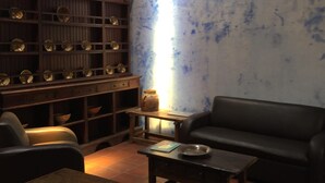 Ein Wohnzimmer mit einem dunkelbraunen Ledersofa, einem Holztisch und einem Bücherregal voller dekorativer Gegenstände.