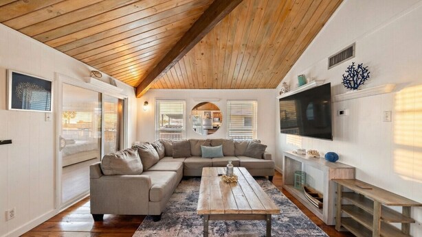 Een ruime woonkamer met een houten plafond, een grote hoekbank, een salontafel en een tv op een houten dressoir.