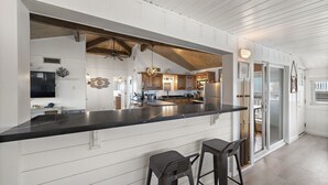 Een moderne keuken met een centraal eiland, witte paneelwanden en een houten plafond.