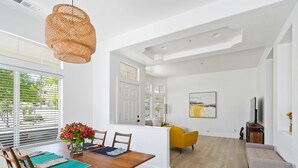 Un vaste espace de vie comprenant une table à manger, des chaises, un fauteuil jaune, un banc et un téléviseur.