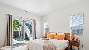 Une chambre à coucher comprenant un lit, une table de chevet, une commode, une chaise et une porte-fenêtre coulissante donnant sur un balcon.