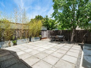 Une terrasse avec une table et des chaises, entourée d’une clôture en bois et agrémentée de différentes plantes.