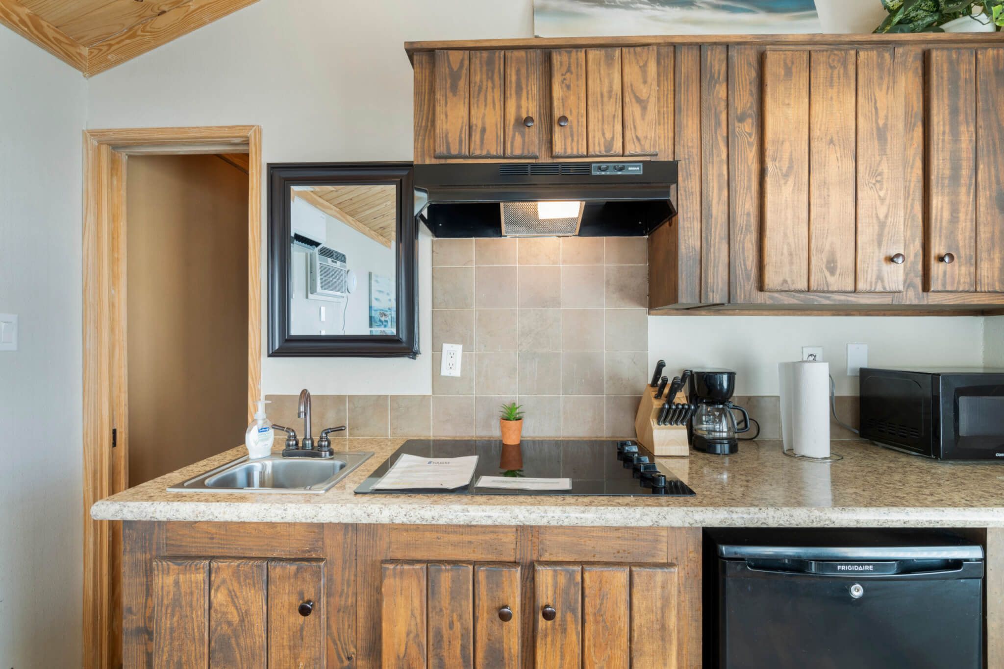A kitchen with wooden cabinets, a stainless steel sink, a black range hood, a coffee maker, and a microwave.