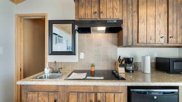 A kitchen with wooden cabinets, a stainless steel sink, a black range hood, a coffee maker, and a microwave.