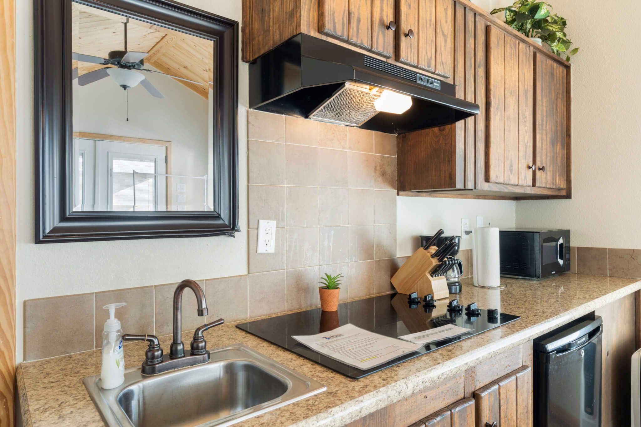 A kitchen with wooden cabinets, a stainless steel sink, a microwave, and a ceiling fan.