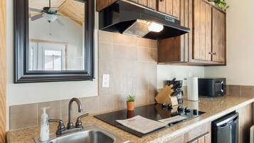A kitchen with wooden cabinets, a stainless steel sink, a microwave, and a ceiling fan.