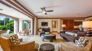 A spacious living area with wicker furniture, a ceiling fan, and a large window overlooking a garden. - I.P.M PRESENTS: VILLA F101 - PRIVATE POOL + YARD! FLEXIBLE CANCELATION POLICY (Kihei)