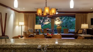 A hotel lobby with a granite reception desk, multiple seating areas, and a view of tropical vegetation through large windows. - I.P.M PRESENTS: VILLA F101 - PRIVATE POOL + YARD! FLEXIBLE CANCELATION POLICY (Kihei)