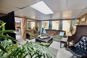 Relax in this stylish living room with a large sofa, armchair, and side table, surrounded by lush greenery and a skylight.