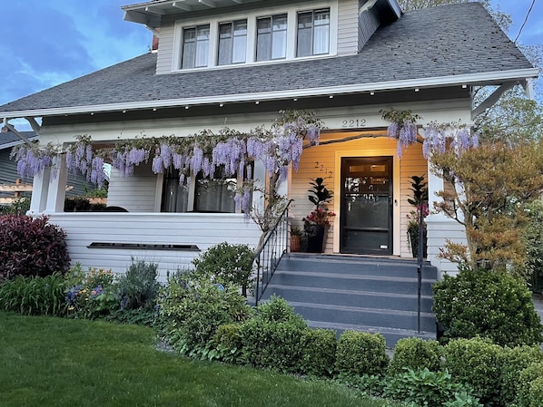 A two-story house with a front porch, number 2212, and purple wisteria hanging over the entrance. - The Wisteria… Beautiful 1915 Craftsman… Close-in, 4 Bdrm, 2 bath (Portland)