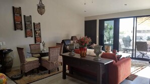 Uma sala de estar ampla com uma mesa de centro de madeira escura, cadeiras de vime, um sofá vermelho e um ventilador de teto.